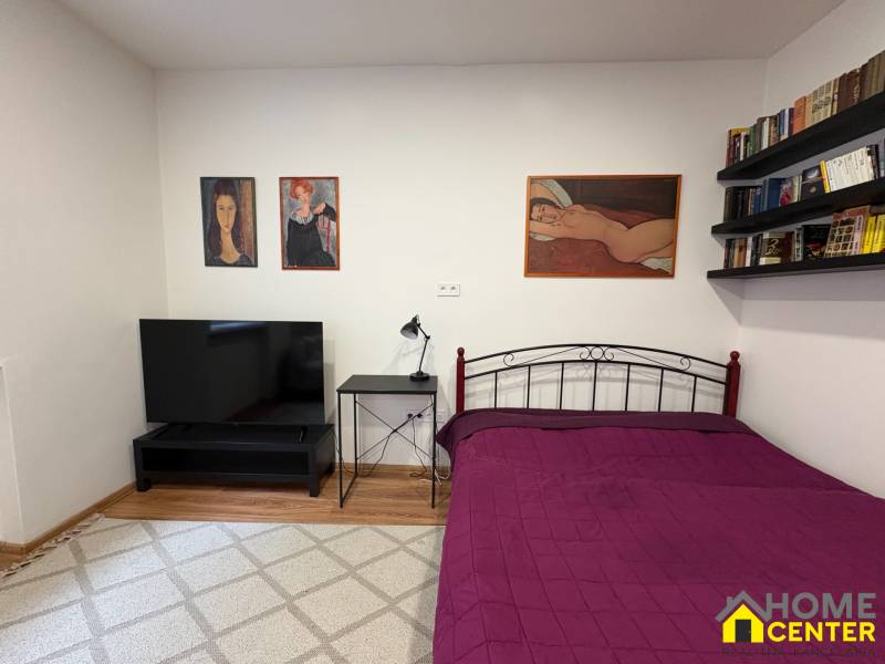 EXKLUZÍVNE na prenájom apartmán s nádychom afrického štýlu v centre KN - Spálňa v 1-izbovom byte s televízorom a obrazmi na strohých stenách.