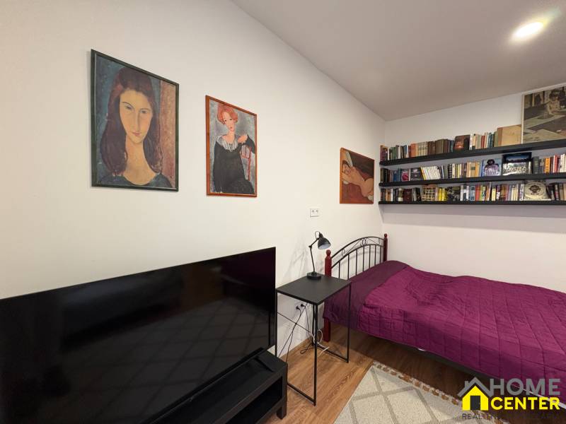 EXKLUZÍVNE na prenájom apartmán s nádychom afrického štýlu v centre KN - Jednoizbový byt s posteľou, policami s knihami a televízorom, podlaha s dreveným dekorom.