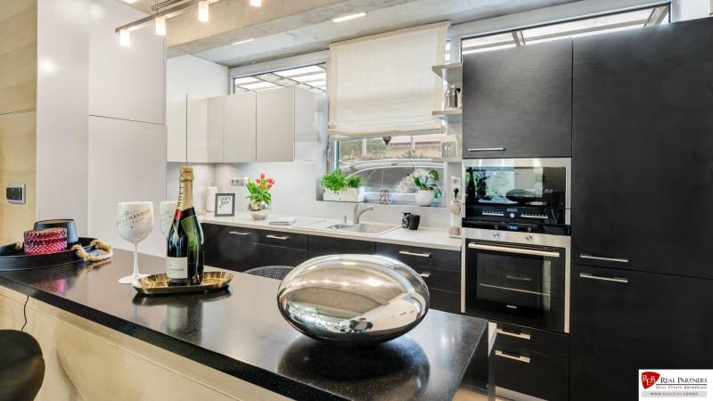 Predaj moderná 5 izbová vila, 265 m2, pozemok 953 m2, bazén,BA II. - Kuchyňa na ulici Imelová a Vila, čierne skrinky, biela linka, okno, dekorácie, kvety.