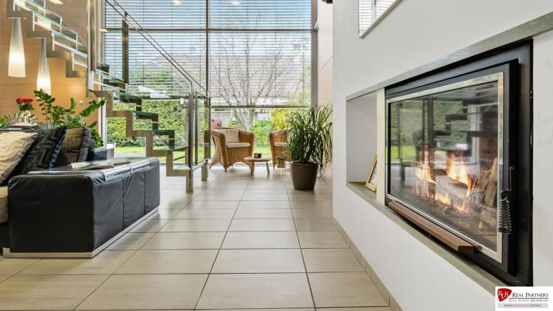 Predaj moderná 5 izbová vila, 265 m2, pozemok 953 m2, bazén,BA II. - Obývačka má krb, schody, čierny gauč; výhľad na ulicu Imelová, Vila a záhrada.