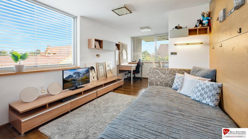 Predaj moderná 5 izbová vila, 265 m2, pozemok 953 m2, bazén,BA II. - Interiér izby na ulici Imelová s pohovkou, stolíkom a písacím stolom vedľa okna.