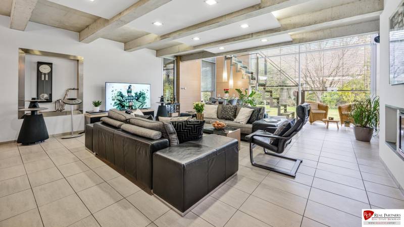 Predaj moderná 5 izbová vila, 265 m2, pozemok 953 m2, bazén,BA II. - Obývačka s veľkým oknom, pohodlnými sedačkami a schodiskom; pohľad na záhradu.