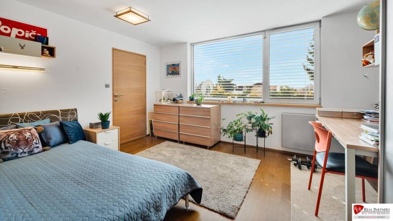 Predaj moderná 5 izbová vila, 265 m2, pozemok 953 m2, bazén,BA II. - Spálňa v dome na ulici Imelová s posteľou, stolom, rastlinami a dreveným nábytkom.