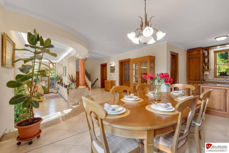 Predaj luxusná 5 izbová Vila,440 m2,pozemok 1061m2,garáž,bazén,BA II. - Jedáleň vo vile so stolom, rastlinou a schodiskom na ulici Hrušovská.