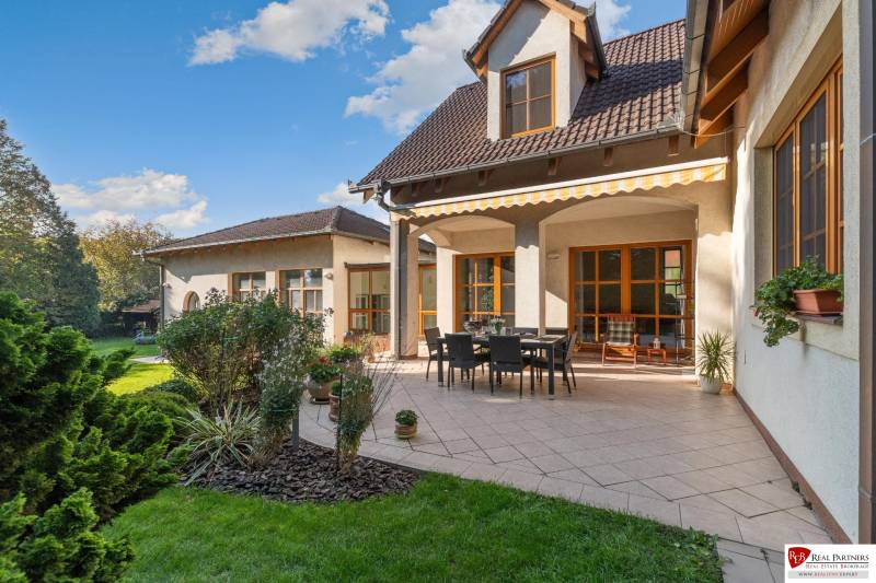 Predaj luxusná 5 izbová Vila,440 m2,pozemok 1061m2,garáž,bazén,BA II. - Vila na ulici Hrušovská s terasou, záhradkou, obdĺžnikovým stolom a stoličkami pod markízou.