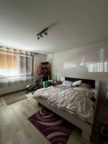 Rodinný dom s prístavbou na  podnikanie – Tešedíkovo - Spálňa s posteľou, cvičebnými strojmi, knihovničkou a podlahou s dreveným dekorom v rodinnom dome.