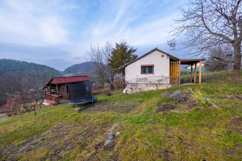 CHATKA SO ZÁHRADOU, PREŠOV – ŠIDLOVEC - Chata v Prešove obklopená stromami, s výhľadom na kopce a trampolínou v záhrade.