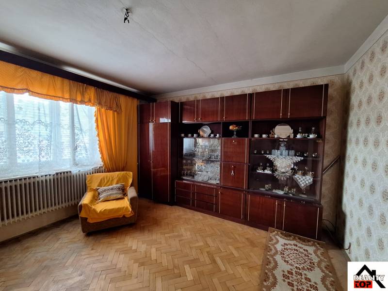 Výborný rodinný dom pre pohodlné bývanie - Obývacia izba v rodinnom dome s kreslom, nábytkom a podlahou s dreveným dekorom.