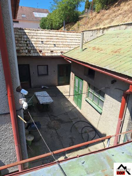 Výborný rodinný dom pre pohodlné bývanie - Dvor rodinného domu v Tachtoch s viditeľnými dverami, stolom a trávnatým svahom.