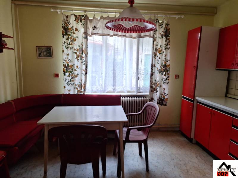 Výborný rodinný dom pre pohodlné bývanie - Kuchyňa v rodinnom dome s červeným nábytkom, farebnými závesmi a plastovými stoličkami.