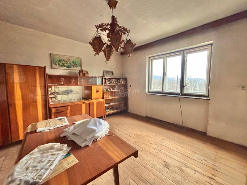 Predaj rodinného domu v Skalitom  - Izba v rodinnom dome s dreveným dekorom, vintage nábytkom, lustrom a veľkým oknom.