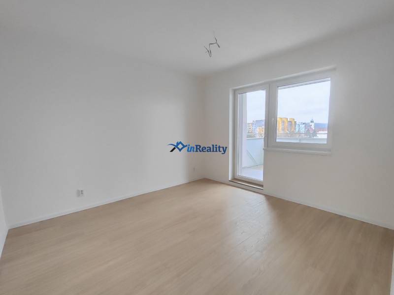  Na predaj moderný 2-izbový byt v Rezidencii Majakovského, Lučenec - Prázdna izba v 2-izbovom byte s podlahou s dreveným dekorom a balkónovými dverami.