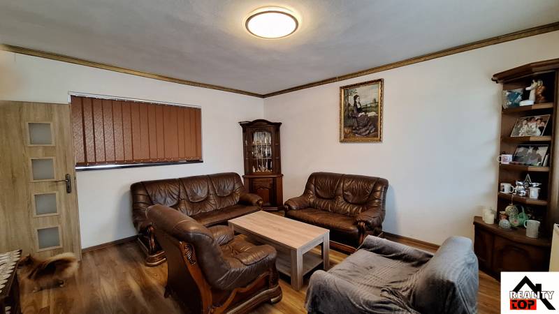 Investujte do budúcnosti - Obývačka v rodinnom dome s koženými sedacími súpravami a podlahou s dreveným dekorom.