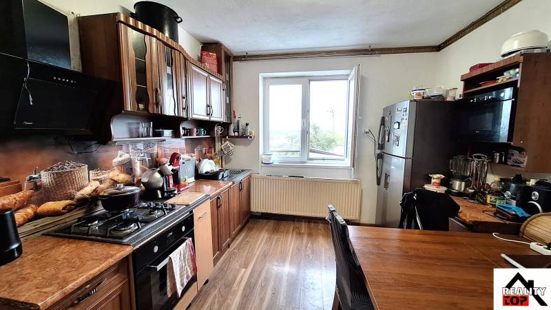 Investujte do budúcnosti - Kuchyňa rodinného domu s kuchynskou linkou, spotrebičmi a podlahou s dreveným dekorom.