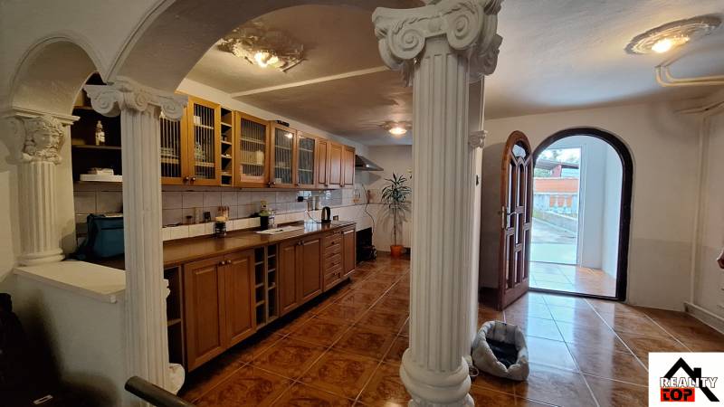 Investujte do budúcnosti - Interiér rodinného domu s drevenou kuchynskou linkou, stĺpmi a podlahou s dreveným dekorom.