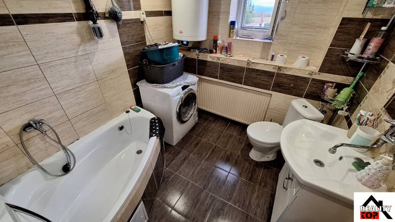 Investujte do budúcnosti - Kúpeľňa v rodinnom dome s vaňou, práčkou a dekoratívnymi hnedými obkladmi.