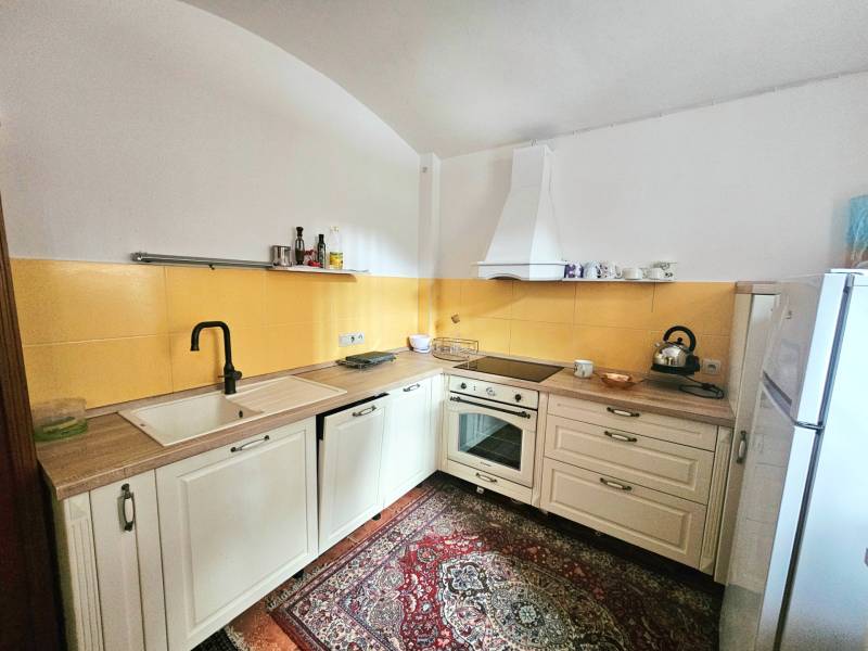  Veľkometrážny 3 izbový byt v kúpeľnom meste Trenčianske Teplice  - Kuchyňa v 3-izbovom byte s krémovými skrinkami, žltým obkladom a vzorovaným kobercom.