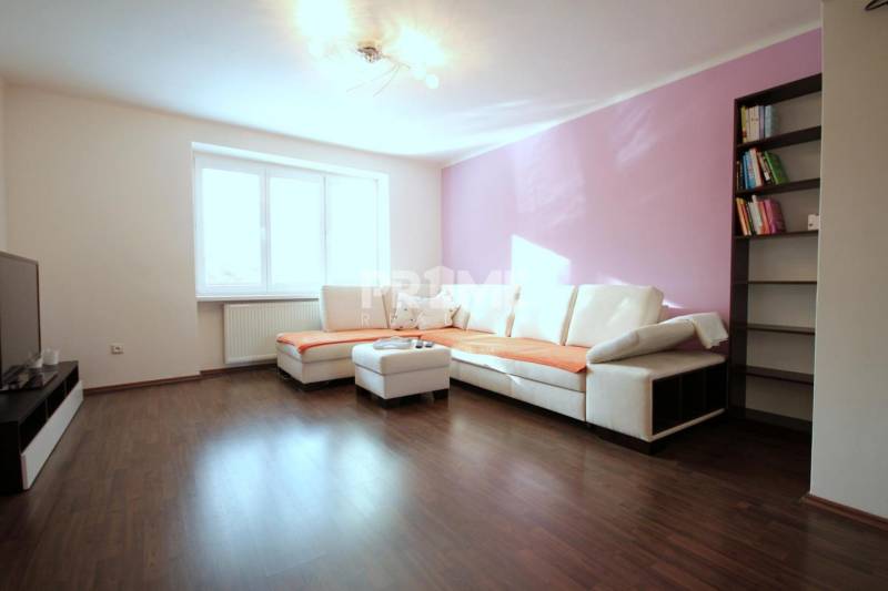 Moderný 2i byt, balkón, tehla, tichá lokalita, Kadnárova ul., Rača - Obývačka 2-izbového bytu s rohovou sedačkou, knižnicou a podlahou s dreveným dekorom.