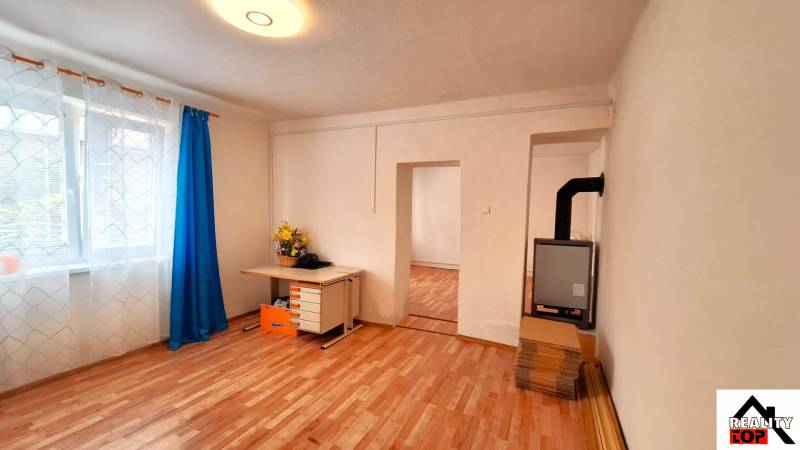 Rodinný dom po čiastočnej rekonštrukcii - Rodinný dom s podlahou s dreveným dekorom, okno so záclonami a písací stôl.