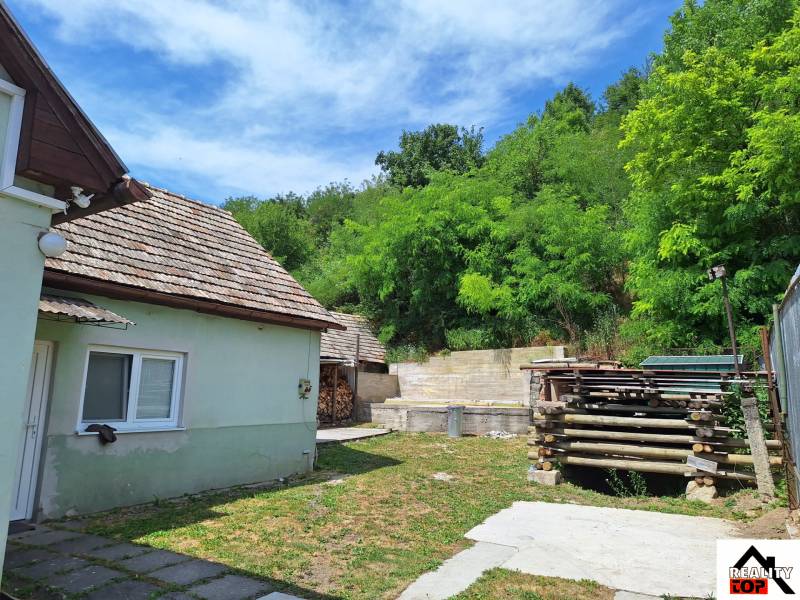 Rodinný dom po čiastočnej rekonštrukcii - Rodinný dom v Hajnáčke s dvorom, drevárňou a zelenými stromami na okolí.