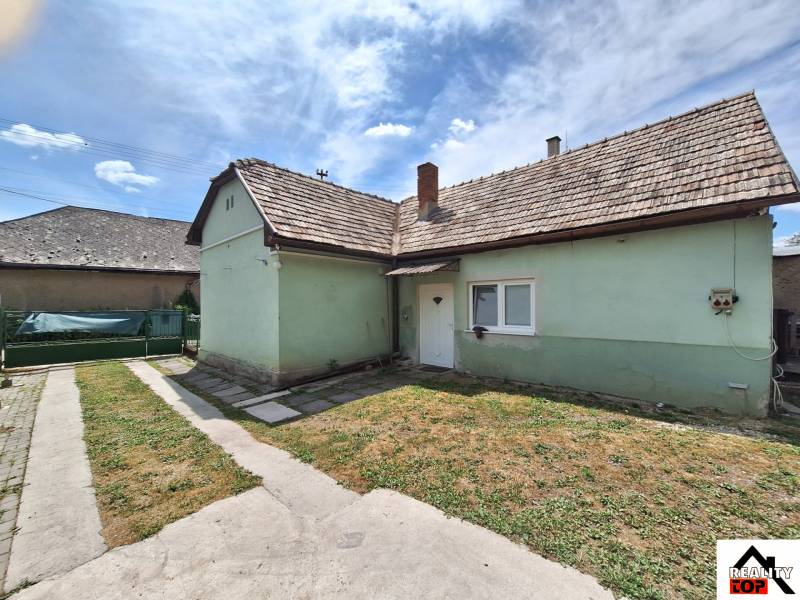 Rodinný dom po čiastočnej rekonštrukcii - Rodinný dom v Hajnáčke s asfaltovým chodníkom a zeleným trávnikom pod modrou oblohou.