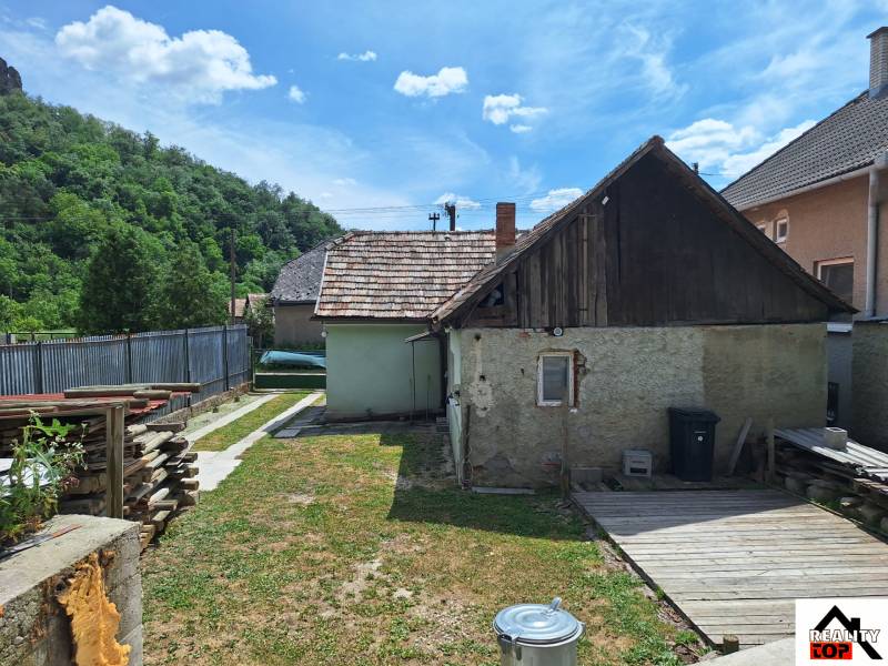 Rodinný dom po čiastočnej rekonštrukcii - Rodinný dom v Hajnáčke s oploteným dvorom, drevenou prístavbou a skladovaným drevom.