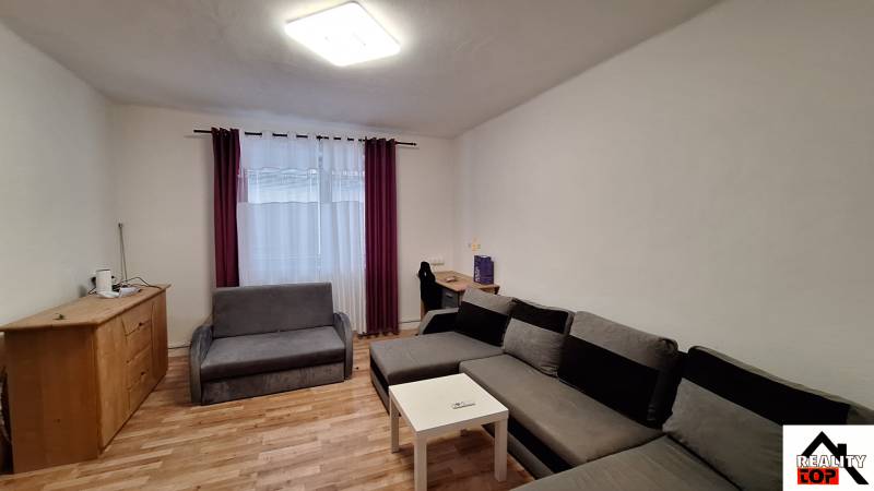 Rodinný dom po čiastočnej rekonštrukcii - Obývačka v rodinnom dome s rohovou sedačkou a podlahou s dreveným dekorom.