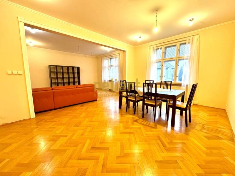 Horský Park:Na prenájom veľkometrážny, 4i, charizmatický byt - Jedáleň so súpravou stolov a stoličiek, vedľa obývačky s oranžovou sedačkou. Podlaha s dreveným dekorom.