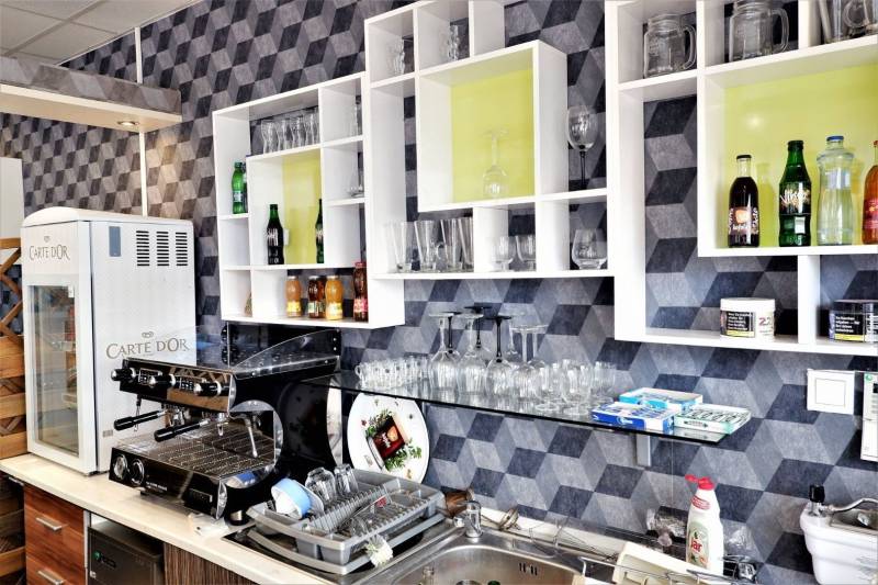 Kaviareň v Top lokalite mesta Šaľa na predaj - Interiér obchodných priestorov s kávovarom, regálmi, pohármi a nápojmi na poličkách.