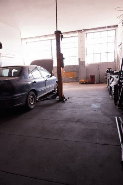 Prevádzková budova-AUTOSERVIS na predaj vo Veľkých Úľanoch - Auto na zdviháku v interiéri výrobných priestorov s veľkými oknami.