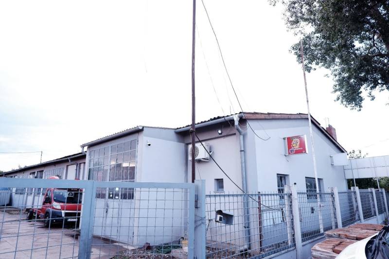 Prevádzková budova-AUTOSERVIS na predaj vo Veľkých Úľanoch - Výrobné priestory v meste Veľké Úľany so šedou fasádou a červeným autom za plotom.