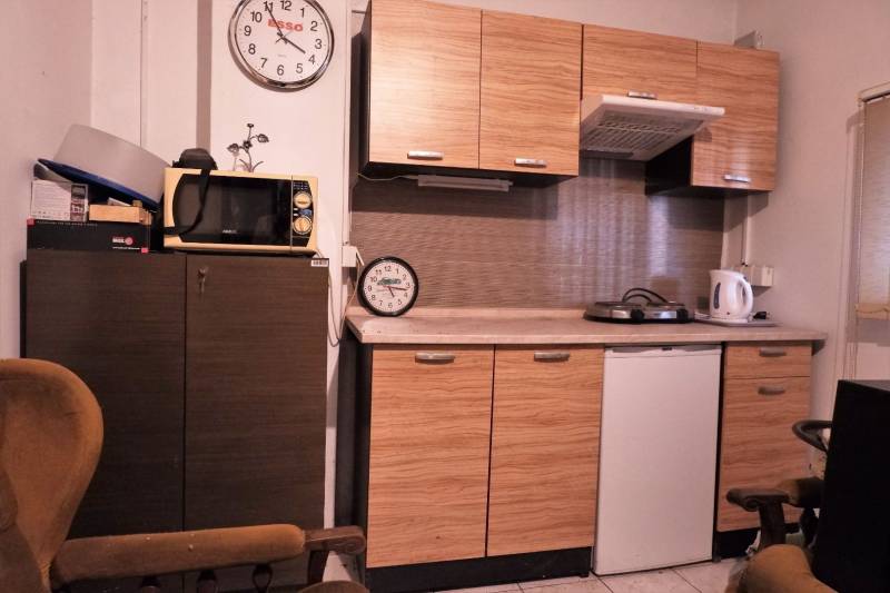 Prevádzková budova-AUTOSERVIS na predaj vo Veľkých Úľanoch - Kuchyňa s dreveným dekorom, mikrovlnkou, dvoma hodinami a spotrebičmi na linke.