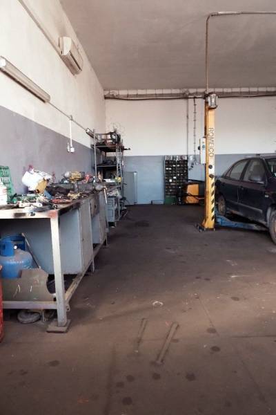 Prevádzková budova-AUTOSERVIS na predaj vo Veľkých Úľanoch - V dielni sú náradia, auto na zdviháku a roztrúsené diely na podlahe.