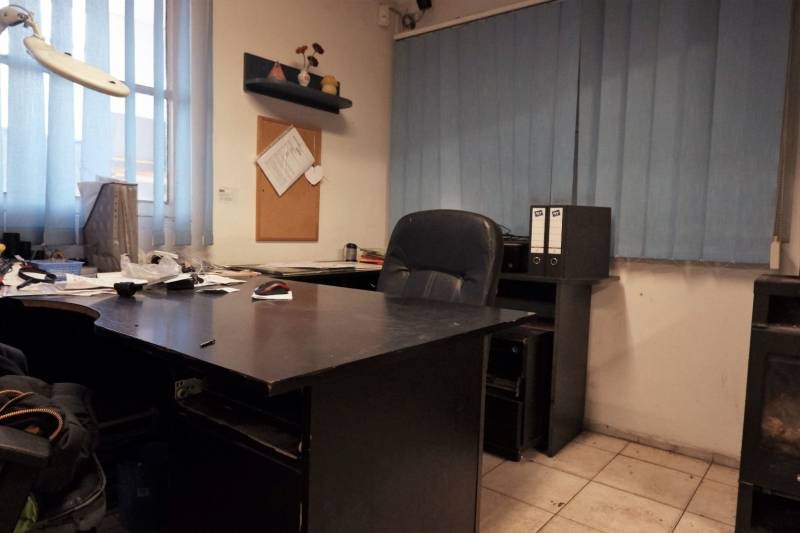 Prevádzková budova-AUTOSERVIS na predaj vo Veľkých Úľanoch - Kancelária s tmavým stolom, dlažbou a modrými vertikálnymi žalúziami vo výrobných priestoroch.