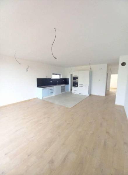 POSLEDNÁ Novostavba 4-izb rodinného domu v lukratívnej časti mesta - Kuchyňa s bielymi skrinkami, tmavou pracovnou doskou a podlahou s dreveným dekorom.