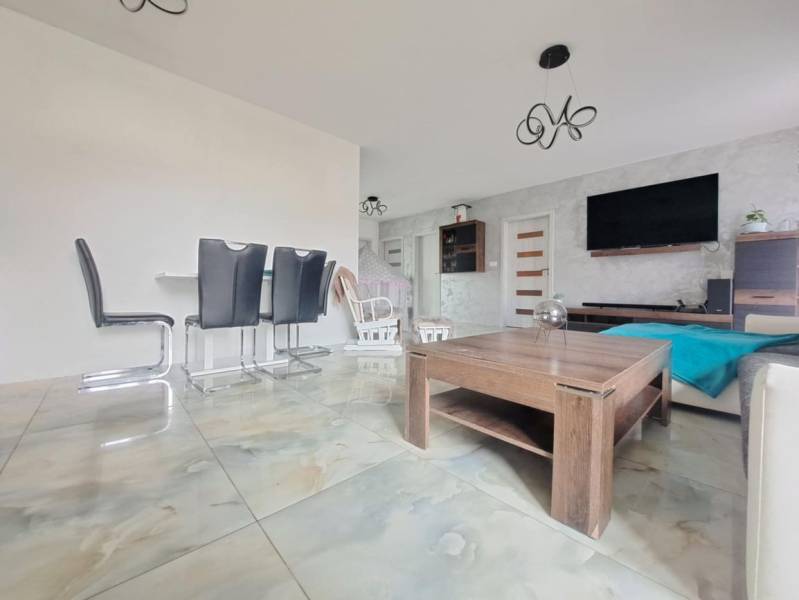 Neodolateľná ponuka! 4-izbová novostavba Galanta-Kolónia za super cenu - Interiér rodinného domu so svetlými dlaždicami, moderným nábytkom a stenou s televízorom.