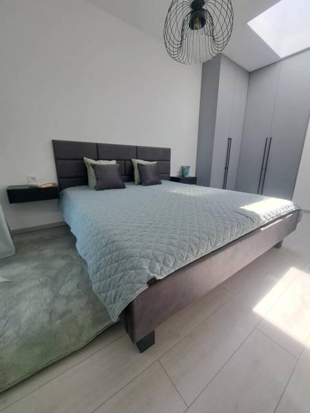 SKOLAUDOVANÉ! Novostavba 2,3 izbových bytov a nebytových priestorov - Spálňa s veľkou posteľou, sivými skriňami a čiernym lustrom v 2-izbovom byte.