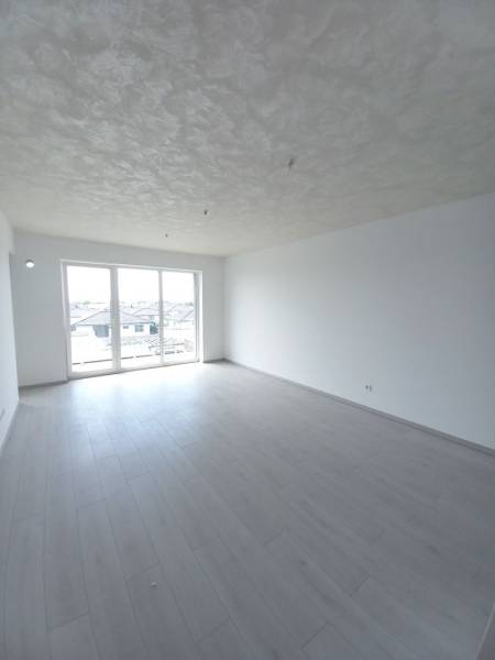 SKOLAUDOVANÉ! Novostavba 2,3 izbových bytov a nebytových priestorov - Svetlá miestnosť s podlahou s dreveným dekorom a veľkými oknami v 2-izbovom byte.