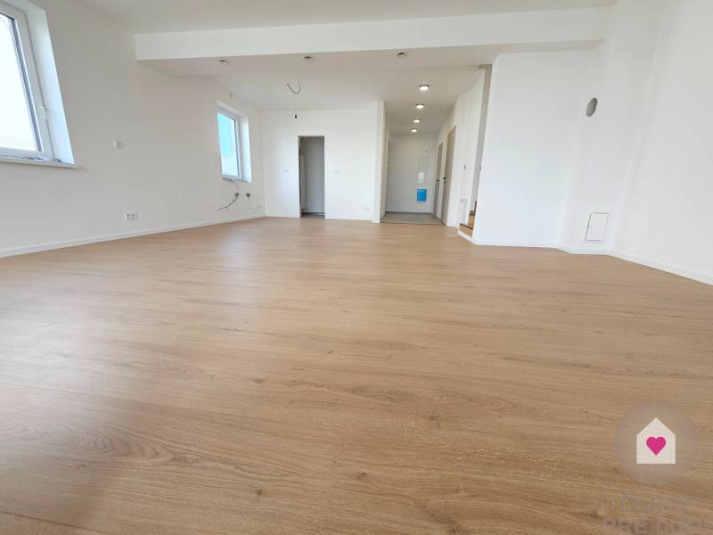 VEĽKORYSO RIEŠENÝ 4 izbový RD-128 m2 S TEP. ČERPADLOM, POZEMOK 405 m2 - Priestranná izba v rodinnom dome s podlahou s dreveným dekorom a bielymi stenami.