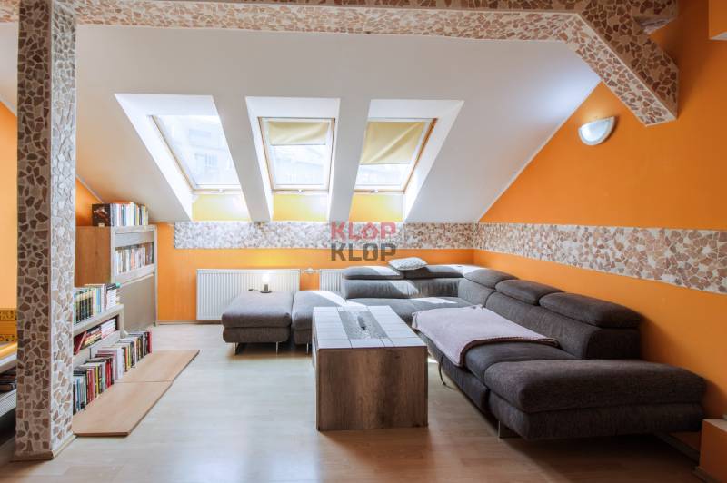 Kúpte si veľký PODKROVNÝ 4i BYT so ZÁHRADOU a PIVNICOU v Starom meste - Podkrovná obývačka s oranžovými stenami, šedou sedačkou a knižnicou v 4-izbovom byte.