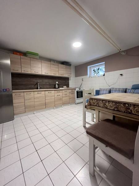 Dvojpodlažný 5i RD pri Dunajskej Strede, 55 min od BA - Kuchyňa v rodinnom dome s dlažbou, drevenými skrinkami, chladničkou a jedálenským stolom.