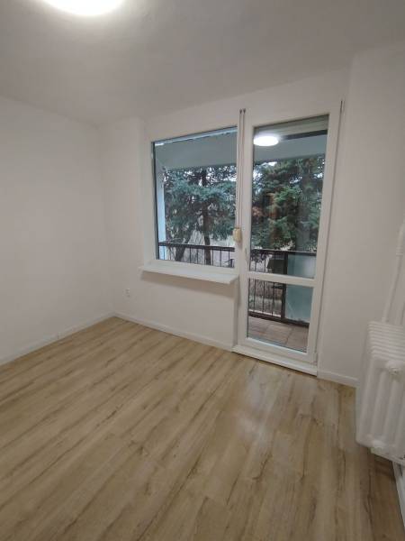  Na predaj  3i byt s vlastnou garážou neďaleko Šale - Izba so svetlými stenami, podlahou s dreveným dekorom a výhľadom na zeleň.