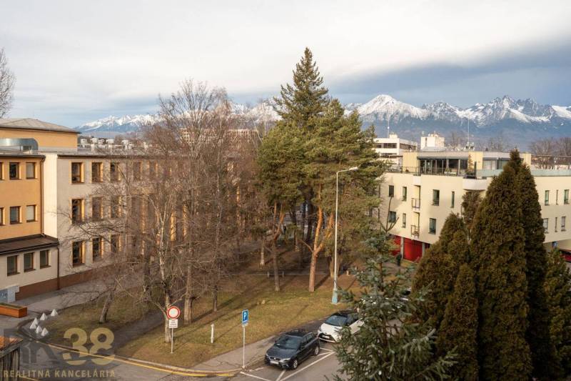 Rezervované: Na predaj pekný 2-izbový byt v centre mesta Poprad - Výhľad na zasnežené Tatry z Murgašovej ulice v Poprade, obklopené zeleňou a budovami.