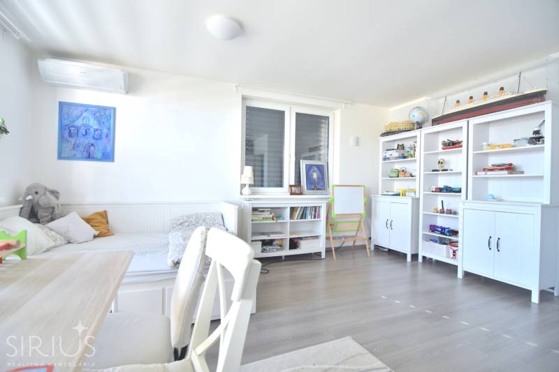 HROZNOVÁ, 4-i RD, 161 m2 – novostavba, krb, klíma, krásna záhrada - Svetlá izba v rodinnom dome s poličkami, stolom, sedačkou a dekoráciami na podlahe s dreveným dekorom.