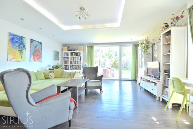 HROZNOVÁ, 4-i RD, 161 m2 – novostavba, krb, klíma, krásna záhrada - Obývacia izba v rodinnom dome s pohovkou, kreslom, knižnicou a presklenými dverami.