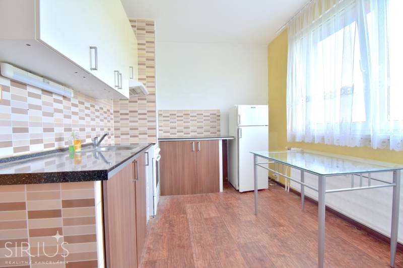 BAKOŠOVA, 1-i byt, 43 m2 – nerušený VÝHĽAD NA KARPATY - Kuchyňa 1-izbového bytu s podlahou s dreveným dekorom, sklenený stôl a spotrebiče.