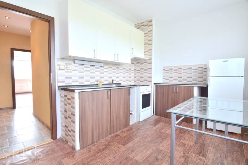 BAKOŠOVA, 1-i byt, 43 m2 – nerušený VÝHĽAD NA KARPATY - Kuchyňa v 1-izbovom byte s podlahou s dreveným dekorom, biele skrinky, sklenený stôl.