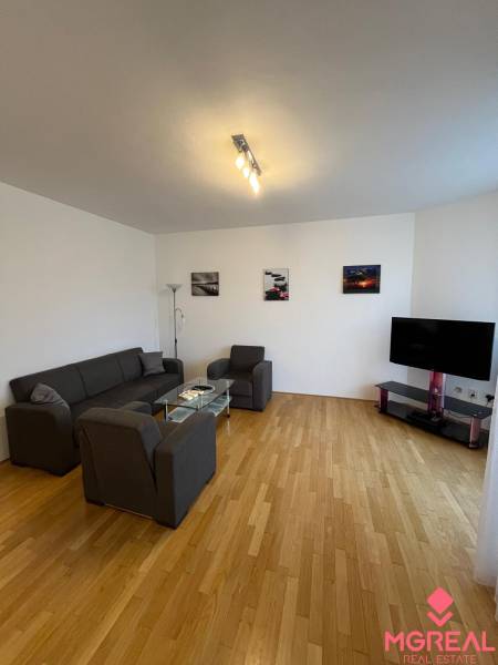 3i byt staršia novostavba, garáž, pivnica, Staré Mesto - Obývacia izba v 3-izbovom byte s podlahou s dreveným dekorom, sedačkou a televízorom.