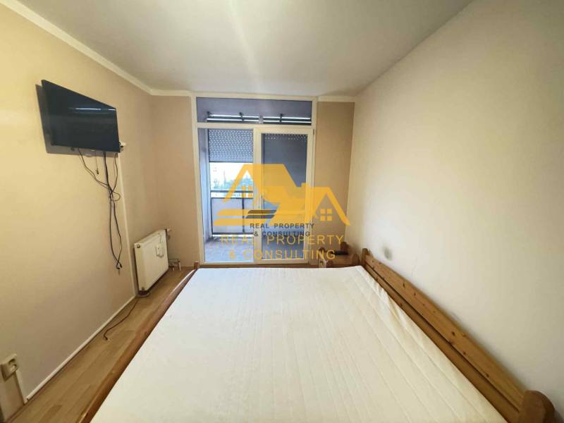 Prenajmem 3 izbový byt na sídlisku Juh v Nových Zámkoch - Spálňa v 3-izbovom byte s posteľou, televízorom na stene a vstupom na balkón.