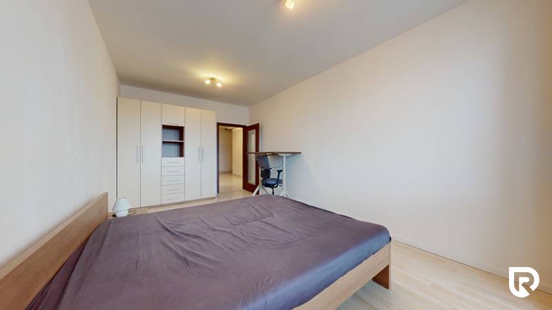 | Svetlý priestranný 2 izbový byt | parkovanie | REZERVOVANÝ - Spálňa v 2-izbovom byte s posteľou, skriňou, stolom a podlahou s dreveným dekorom.